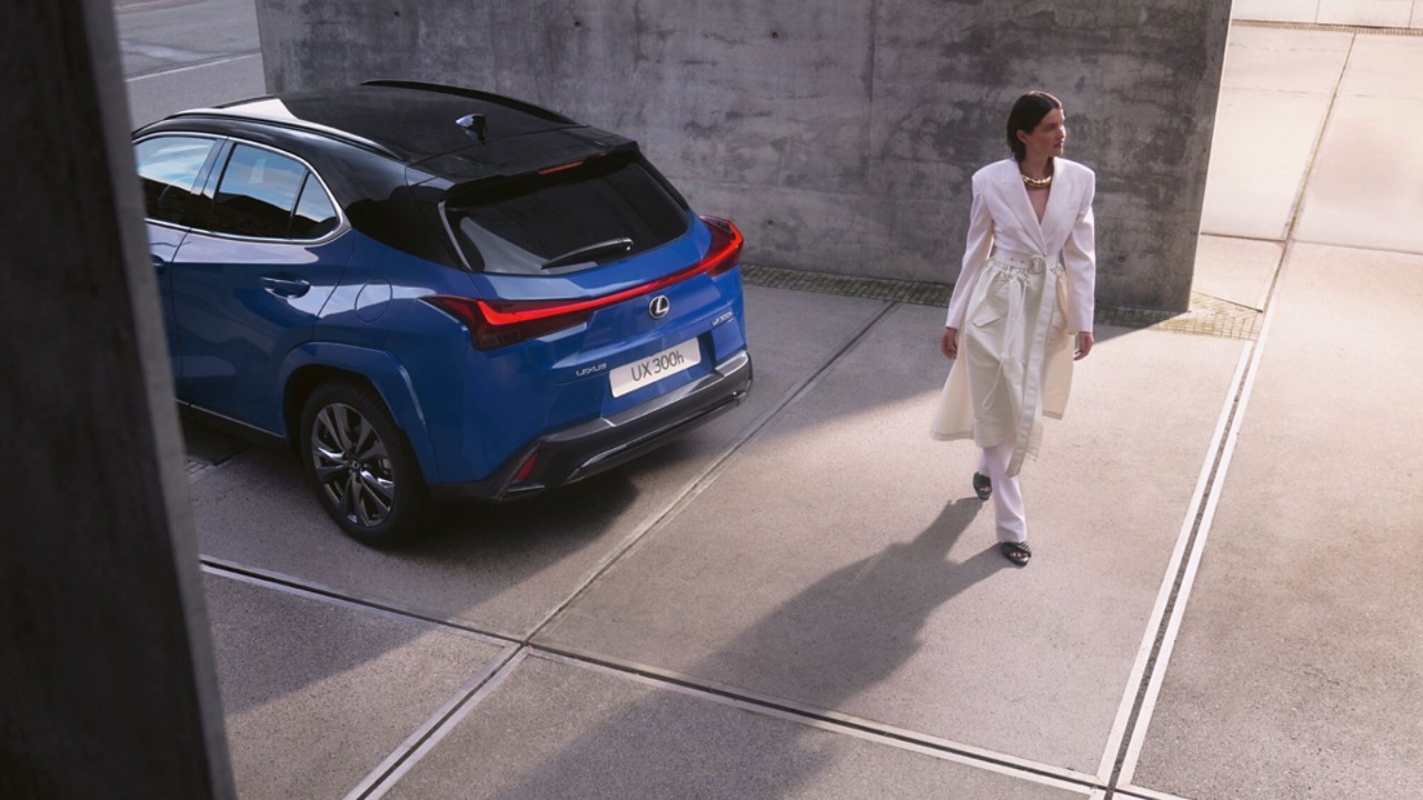 Een persoon staat naast en blauwe Lexus UX