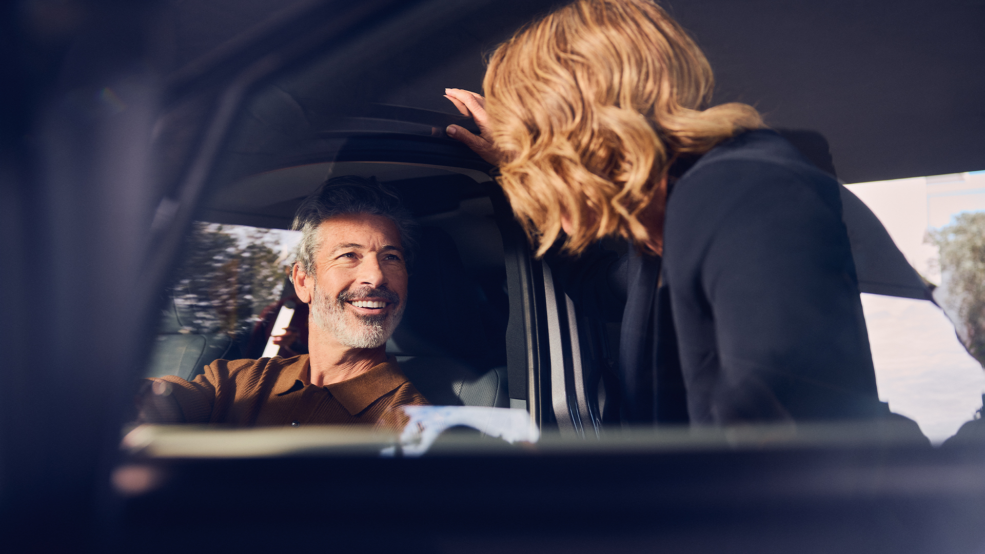 Een bestuurder die glimlacht naar iemand in de deuropening bij een geparkeerde Lexus